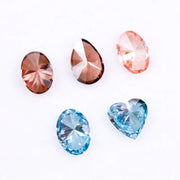 Five loose lab grown diamonds displayed on a white background, featuring three pink diamonds in oval, pear, and round cuts, alongside two vivid blue diamonds in heart and oval shapes, showcasing brilliant faceting and high clarity.