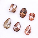Six fancy colored lab grown diamonds in pink, peach, and cognac tones featuring emerald cut, oval cut, and pear cut shapes displayed on a white background, ethical CVD loose stones for custom fine jewelry.