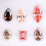 Six fancy colored lab grown diamonds including pear, marquise, and emerald cuts in pink, peach, champagne, and brown tones displayed on a white background, ideal for custom engagement rings and fine jewelry.