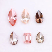 Six fancy colored lab grown diamonds including pear, marquise, and emerald cuts in pink, peach, champagne, and brown tones displayed on a white background, ideal for custom engagement rings and fine jewelry.