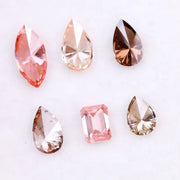 Six fancy colored lab grown diamonds including pear, marquise, and emerald cuts in pink, peach, champagne, and brown tones displayed on a white background, ideal for custom engagement rings and fine jewelry.