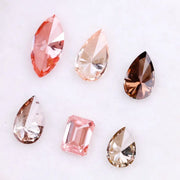 Six fancy colored lab grown diamonds including pear, marquise, and emerald cuts in pink, peach, champagne, and brown tones displayed on a white background, ideal for custom engagement rings and fine jewelry.