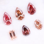 Six lab grown fancy colored diamonds in pink, blush, champagne and deep rose tones featuring pear, oval and emerald cuts displayed on a white background for fine jewelry design.