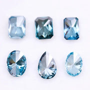 Six lab grown blue diamonds in emerald, oval and pear cuts displaying fancy deep ocean blue color arranged on white background for custom engagement ring and fine jewelry making.