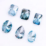 Six lab grown blue diamonds in emerald, oval and pear cuts displaying fancy deep ocean blue color arranged on white background for custom engagement ring and fine jewelry making.
