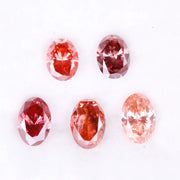 Five oval cut pink lab grown diamonds displayed on a white background, ranging in color from light blush pink to deep vivid rose and red tones, shown for color comparison and gemstone selection.