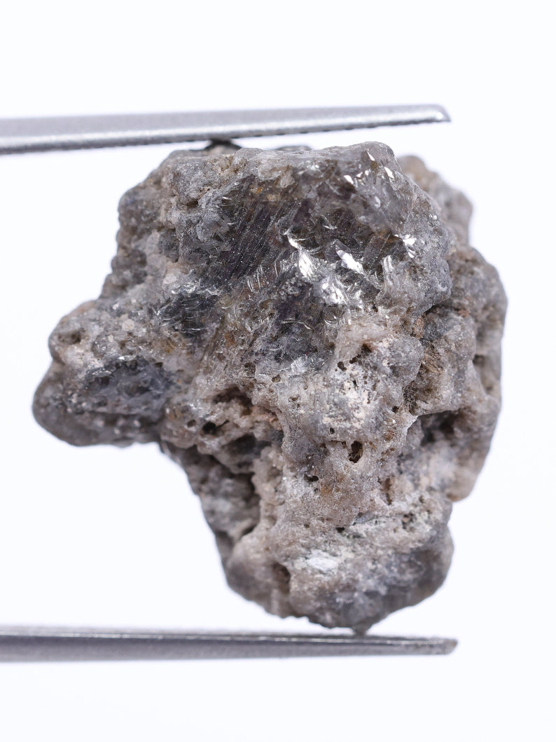 Raw diamond held by tweezers on a white background