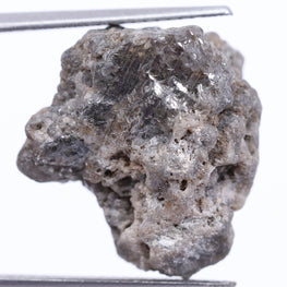 Raw diamond held by tweezers on a white background