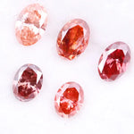 Five oval cut pink lab grown diamonds displayed on a white background, ranging in color from light blush pink to deep vivid rose and red tones, shown for color comparison and gemstone selection.