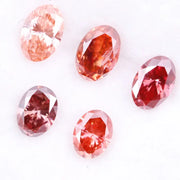 Five oval cut pink lab grown diamonds displayed on a white background, ranging in color from light blush pink to deep vivid rose and red tones, shown for color comparison and gemstone selection.