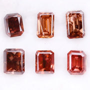 Six lab grown fancy orange pink emerald cut diamonds displayed on a white background, rectangular step cut loose grown diamonds in various reddish peach shades for engagement rings and fine jewelry.