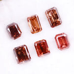 Six lab grown fancy orange pink emerald cut diamonds displayed on a white background, rectangular step cut loose grown diamonds in various reddish peach shades for engagement rings and fine jewelry.