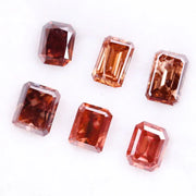 Six lab grown fancy orange pink emerald cut diamonds displayed on a white background, rectangular step cut loose grown diamonds in various reddish peach shades for engagement rings and fine jewelry.