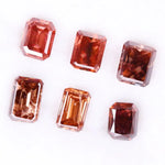 Six lab grown fancy orange pink emerald cut diamonds displayed on a white background, rectangular step cut loose grown diamonds in various reddish peach shades for engagement rings and fine jewelry.