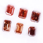 Six lab grown fancy orange pink emerald cut diamonds displayed on a white background, rectangular step cut loose grown diamonds in various reddish peach shades for engagement rings and fine jewelry.