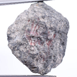 Raw diamond held between tweezers on a white background