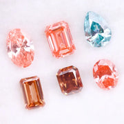 Lab grown fancy pink, peach, cognac and blue diamonds in oval, emerald and pear cuts displayed on white background, sustainable CVD created gemstones for fine jewelry.