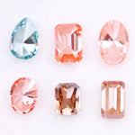 Lab grown fancy pink, peach, cognac and blue diamonds in oval, emerald and pear cuts displayed on white background, sustainable CVD created gemstones for fine jewelry.