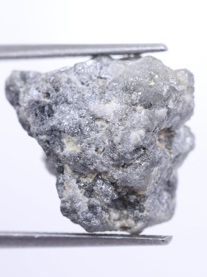 Raw diamond held by tweezers on a white background