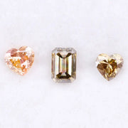 Three lab grown fancy color diamonds including pink heart cut, champagne emerald cut, and yellow heart shape loose diamonds for engagement ring and custom jewelry making