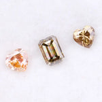 Three lab grown fancy color diamonds including pink heart cut, champagne emerald cut, and yellow heart shape loose diamonds for engagement ring and custom jewelry making