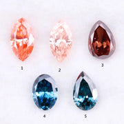 Collection of fancy color lab grown diamonds including pink marquise cut, light peach marquise, brown pear shape, blue oval cut and blue pear cut loose diamonds displayed on white background