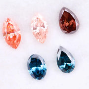 Collection of fancy color lab grown diamonds including pink marquise cut, light peach marquise, brown pear shape, blue oval cut and blue pear cut loose diamonds displayed on white background