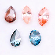 Collection of fancy color lab grown diamonds including pink marquise cut, light peach marquise, brown pear shape, blue oval cut and blue pear cut loose diamonds displayed on white background