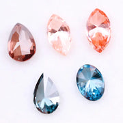 Collection of fancy color lab grown diamonds including pink marquise cut, light peach marquise, brown pear shape, blue oval cut and blue pear cut loose diamonds displayed on white background