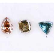 Three fancy color lab grown diamonds including pear cut pink diamond, asscher cut olive diamond, and trillion cut blue diamond displayed on white background for custom jewelry making