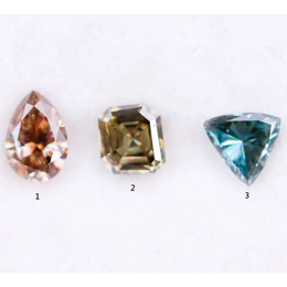 Three fancy color lab grown diamonds including pear cut pink diamond, asscher cut olive diamond, and trillion cut blue diamond displayed on white background for custom jewelry making