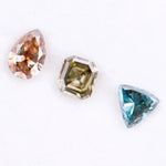 Three fancy color lab grown diamonds including pear cut pink diamond, asscher cut olive diamond, and trillion cut blue diamond displayed on white background for custom jewelry making