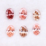 Six oval cut pink lab grown diamonds in varying shades from vivid rose and blush pink to soft peach and champagne, displayed on a white background, showcasing brilliant faceting and exceptional sparkle.