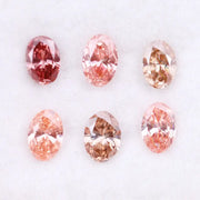 Six oval cut pink lab grown diamonds in varying shades from vivid rose and blush pink to soft peach and champagne, displayed on a white background, showcasing brilliant faceting and exceptional sparkle.