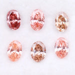 Six oval cut pink lab grown diamonds in varying shades from vivid rose and blush pink to soft peach and champagne, displayed on a white background, showcasing brilliant faceting and exceptional sparkle.