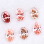 Six oval cut pink lab grown diamonds in varying shades from vivid rose and blush pink to soft peach and champagne, displayed on a white background, showcasing brilliant faceting and exceptional sparkle.