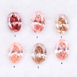 Six oval cut pink lab grown diamonds in varying shades from vivid rose and blush pink to soft peach and champagne, displayed on a white background, showcasing brilliant faceting and exceptional sparkle.