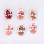 Six oval cut pink lab grown diamonds in varying shades from vivid rose and blush pink to soft peach and champagne, displayed on a white background, showcasing brilliant faceting and exceptional sparkle.