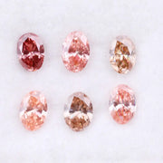 Six oval cut pink lab grown diamonds in varying shades from vivid rose and blush pink to soft peach and champagne, displayed on a white background, showcasing brilliant faceting and exceptional sparkle.