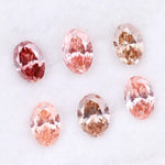 Six oval cut pink lab grown diamonds in varying shades from vivid rose and blush pink to soft peach and champagne, displayed on a white background, showcasing brilliant faceting and exceptional sparkle.