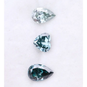 Three blue lab grown diamonds displayed on white background: pear cut light blue diamond (1), heart cut teal diamond (2), and deep blue pear shaped diamond (3), brilliant faceted loose stones for engagement ring or custom fine jewelry.
