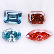 Four fancy color lab grown diamonds including oval and emerald cut blue stones and marquise and radiant cut red gemstones displayed on a white background.