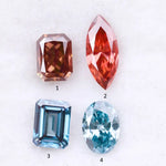 Four fancy color lab grown diamonds including oval and emerald cut blue stones and marquise and radiant cut red gemstones displayed on a white background.
