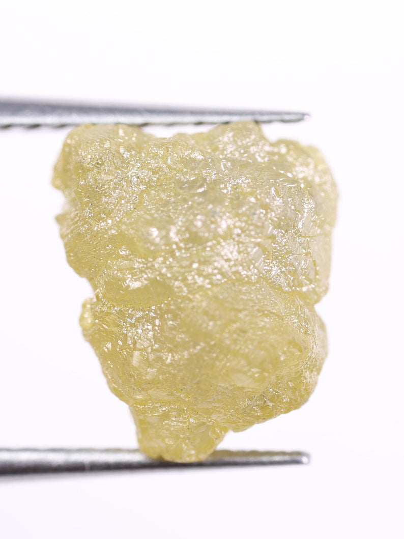 Raw diamond held between tweezers on a white background