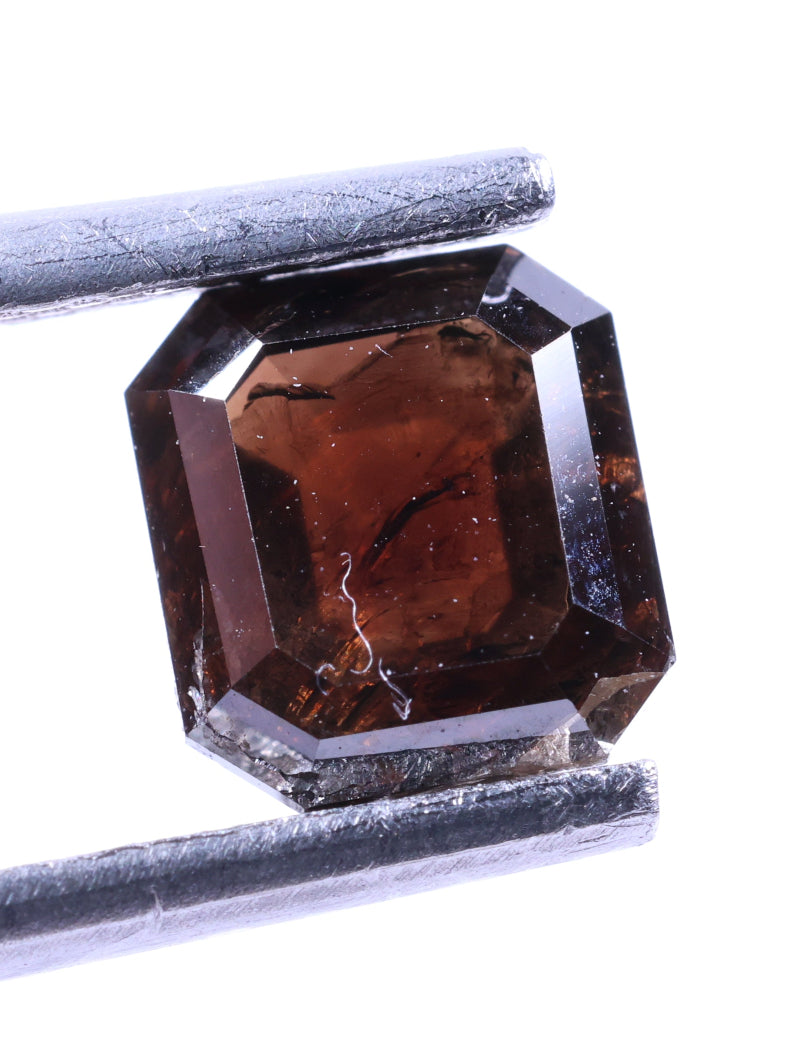 Brown diamond held by tweezers on a white background
