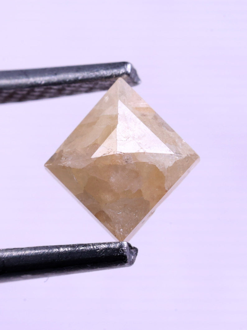 kite shape Diamond held between tweezers against a light purple background
