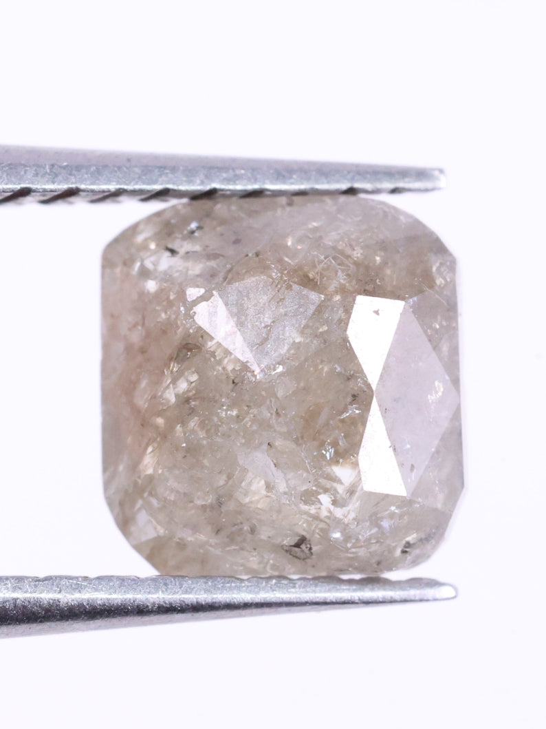 Cushion Cut diamond held between tweezers on a white background