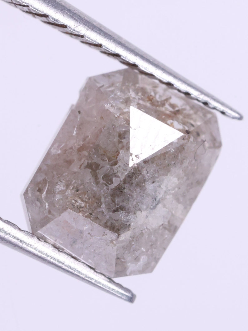 loose diamond held between tweezers on a light purple background
