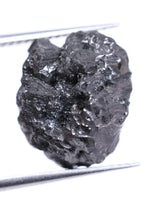 Raw diamond held between tweezers on a white background