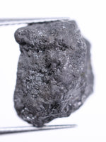 Raw diamond held by tweezers on a white background